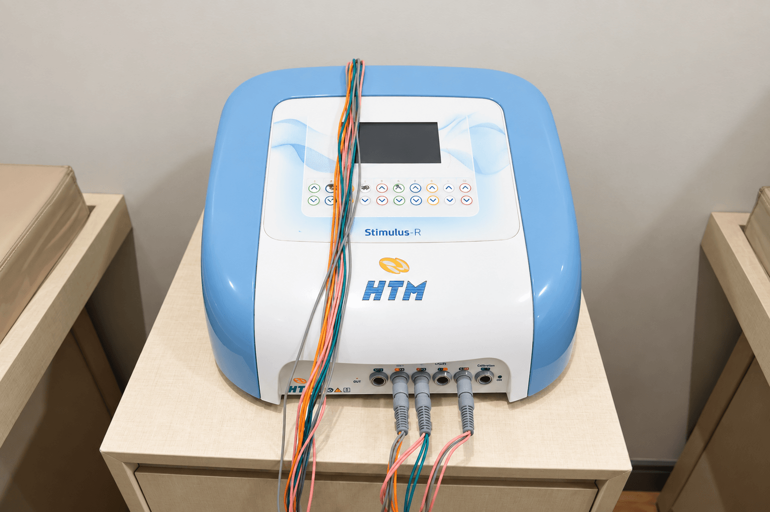 Aparelho de eletroestimulação HTM Stimulus R com cabos coloridos, sobre mesa auxiliar na sala de fisioterapia da Focus Saúde em Ribeirão Preto.