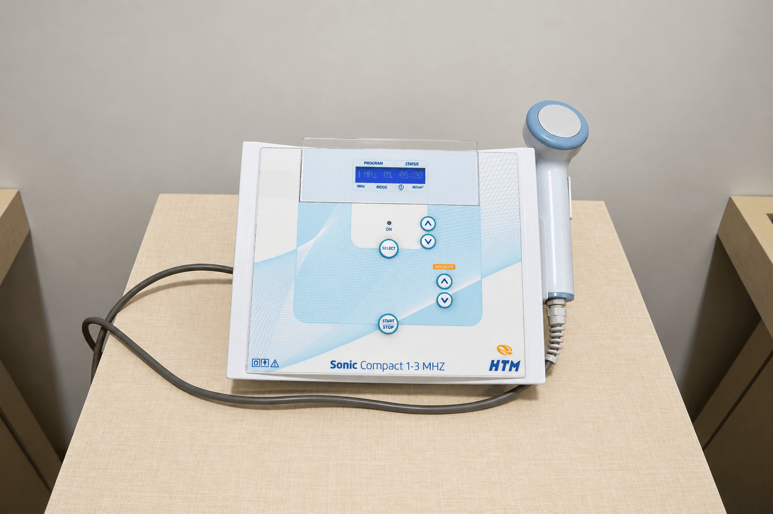 Aparelho de ultrassom terapêutico HTM Sonic Compact 1-3 MHz com transdutor, sobre mesa auxiliar na clínica Focus Saúde em Ribeirão Preto.